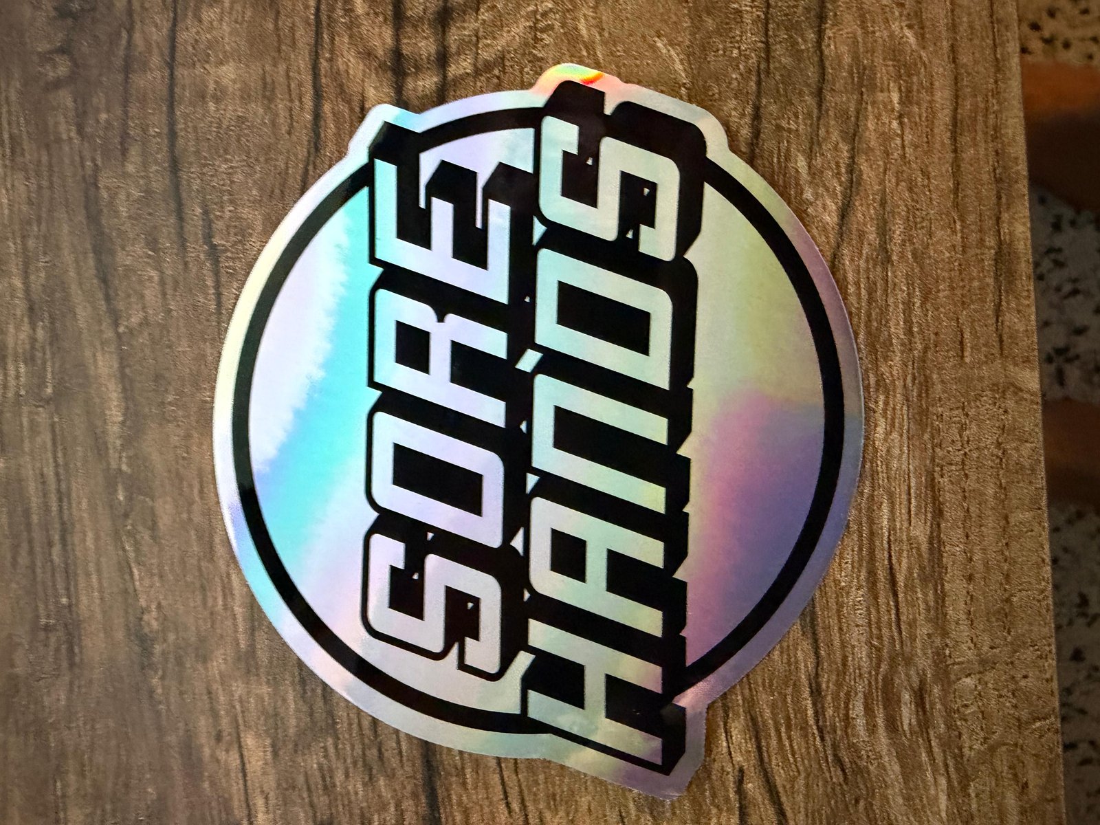 Holographic SORE HANDS sticker close-up. The brand mark in foil.