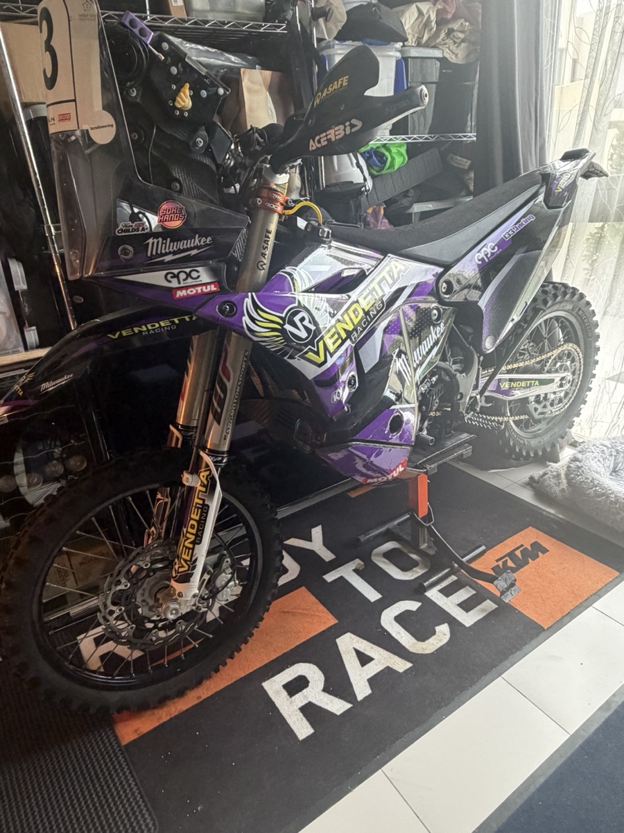 Vendetta Racing rally bike #3 in the Dubai garage. Purple Vendetta livery, Milwaukee sponsor, KTM Ready to Race mat under the wheels.
