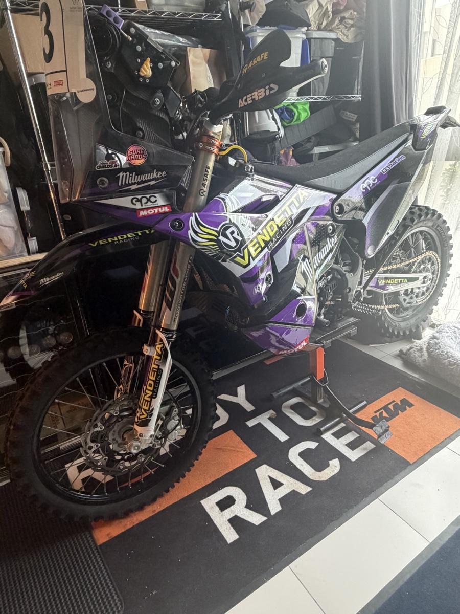 Vendetta Racing rally bike #3 in the Dubai garage. Purple Vendetta livery, Milwaukee sponsor, KTM Ready to Race mat under the wheels.