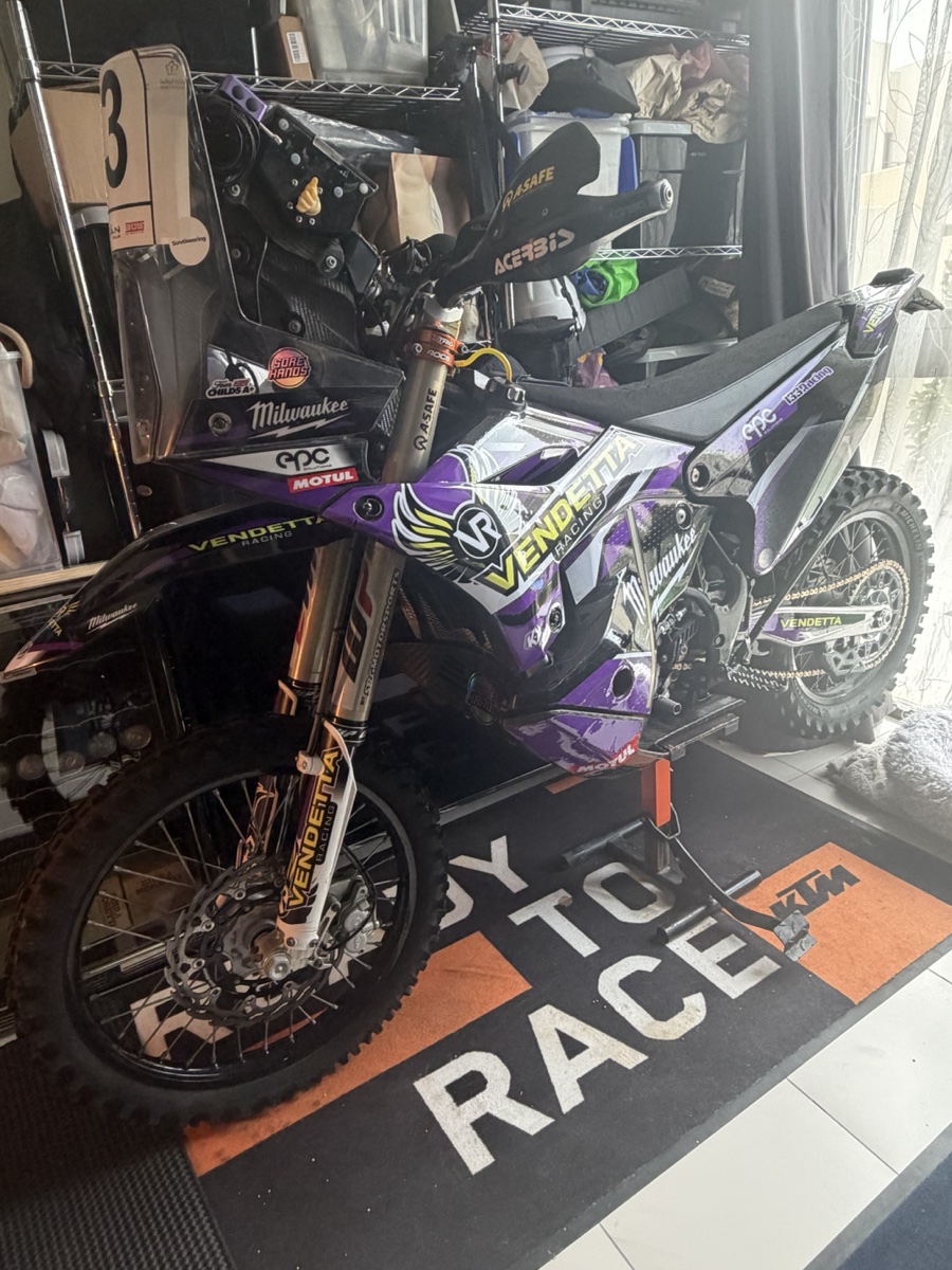 Vendetta Racing rally bike #3 in the Dubai garage. Purple Vendetta livery, Milwaukee sponsor, KTM Ready to Race mat under the wheels.