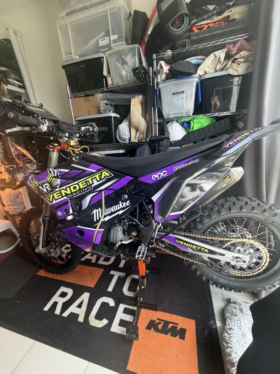 Vendetta Racing rally bike #3 in the Dubai garage. Purple Vendetta livery, Milwaukee sponsor, KTM Ready to Race mat under the wheels.